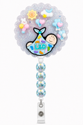 L&D newborn decoden cream badge reel with swaddled baby charm, pastel balloons, sky accents and blue bow beads on a pure white background