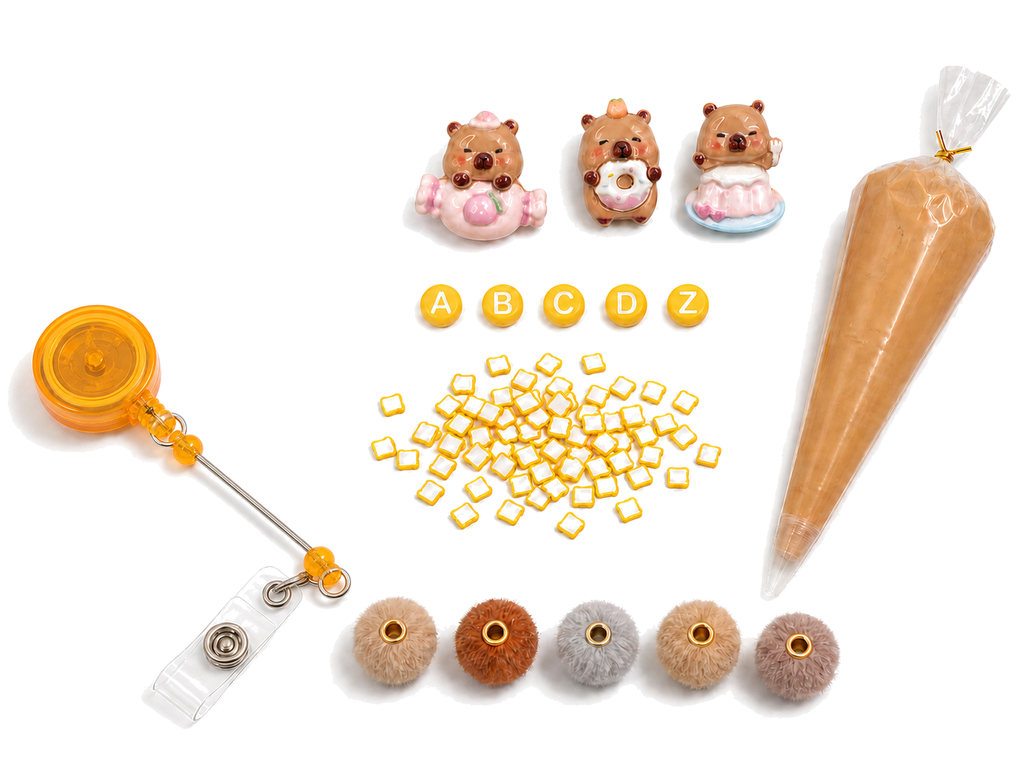 Mini CAPY CAFE DIY badge reel kit with orange default reel, capybara charms, letters, toast pieces, neutral pom-pom beads and caramel cream glue on a pure white background