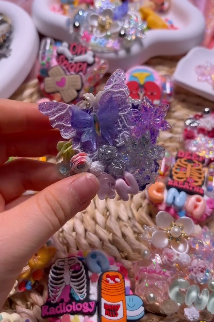 A hand holding a finished ReelCute badge reel above a tray of designs