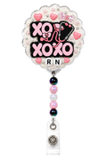 XOXO Nurse RN decoden cream badge reel on a pure white background with stethoscope charm, pink hearts, bow, pearls and pastel beads